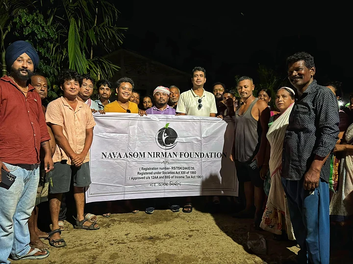Volunteers and residents holding the Nava Asom Nirman Foundation banner at a night relief camp