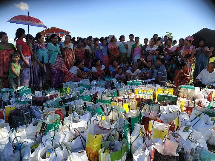Villagers standing behind rows of packed relief kits at a flood relief camp